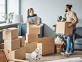 A couple unpacks moving boxes in their new home while their dog sits on the floor