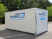 A 1-800-PACK-RAT 16-foot portable storage container sits in an empty parking on a bright sunny day with its side and back facing the viewer