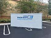 The side view of a 1-800-PACK-RAT portable storage container sitting in the parking lot of a business