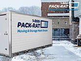 A 1-800-PACK-RAT portable storage container sits in a snowy and icy business parking lot with the 1-800-PACK-RAT logo in the upper right-hand corner of the image