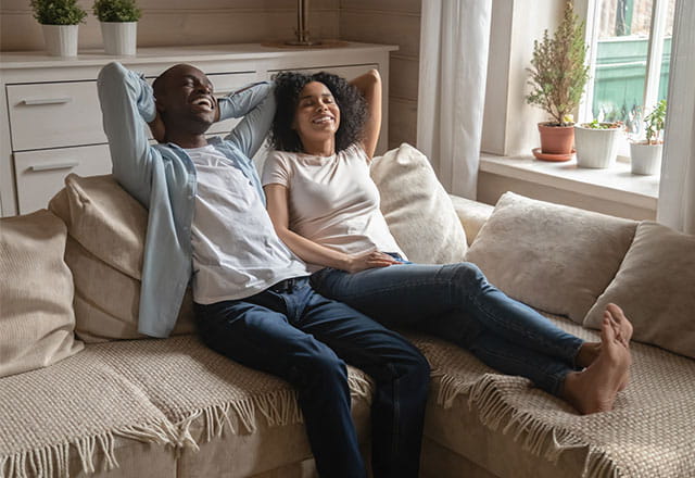 A happy couple sits on a couch in their home