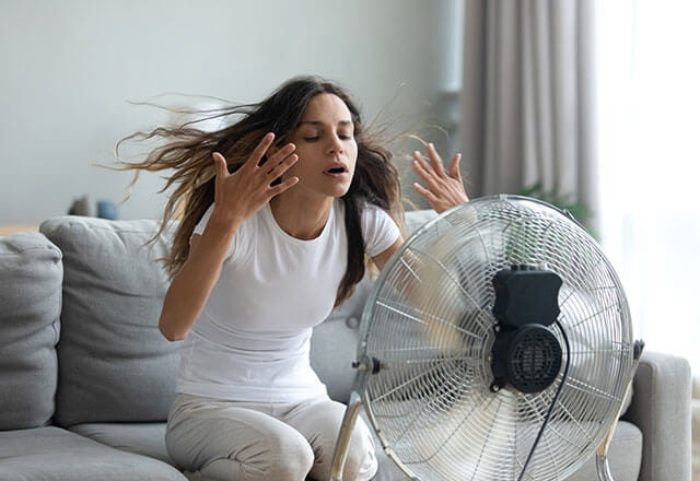 A woman sits in front of a fan to cool herself off