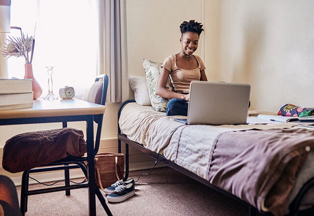 A young woman uses her laptop in her college dorm room