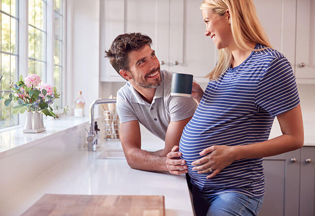 A pregnant woman and her husband talk in their kitchen