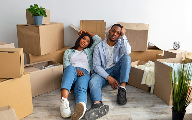 A couple sits on the floor frustrated and surrounded by moving boxes