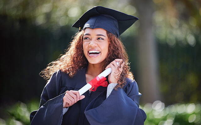 A college graduate smiles while holding her rolled up diploma