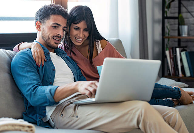 A couple happily looks at their laptop at their home