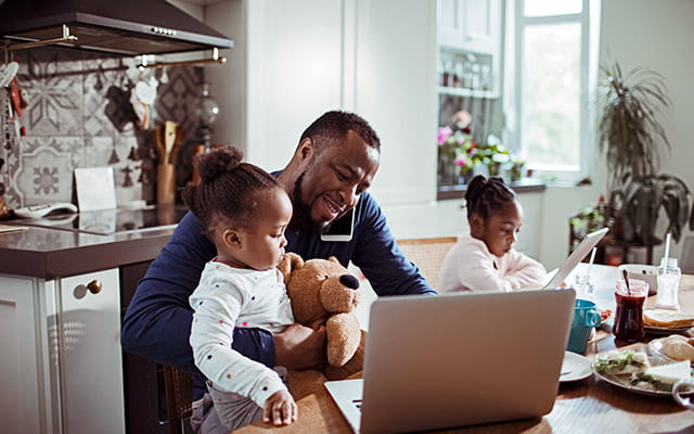 A father sits with his two daughters in their home while on the phone