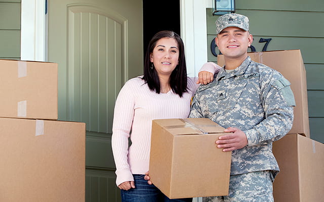 A woman and her military service member husband bring boxes into their new home