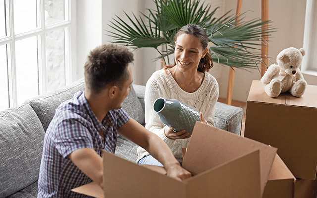 A man and woman pack a vase into a box with other fragile items