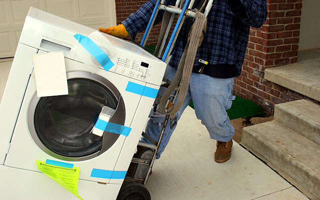 A professional labor worker moves a washing machine out of a home on at heavy duty dolly with wheels