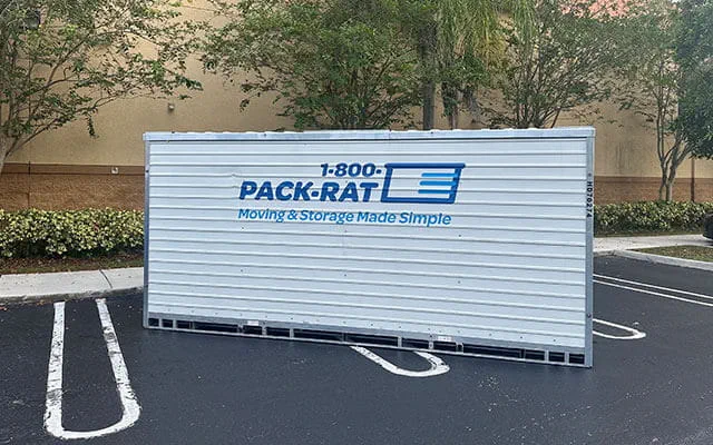 The side view of a 1-800-PACK-RAT portable storage container sitting in the parking lot of a business