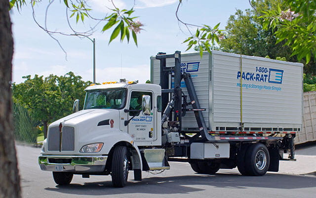 A 1-800-PACK-RAT mini-mover truck is on its way to deliver a portable storage container to a customer