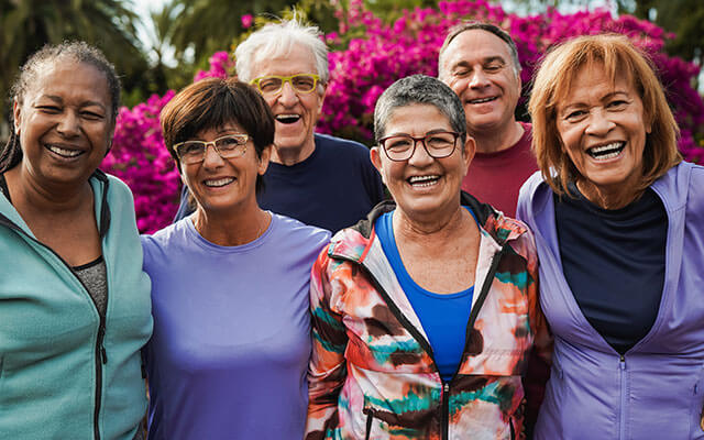 A group of multiracial older adults and friends pose and smile for a photo on a sunny morning