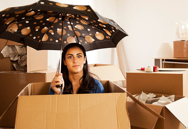 Woman in a box poses with an umbrella while unpacking