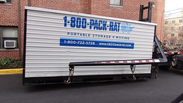 1-800-PACK-RAT Container lowered by truck in driveway.