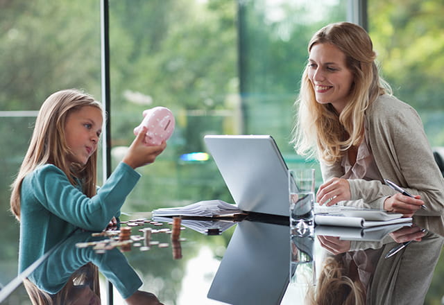 Mom on computer while daughter counts change from piggy bank