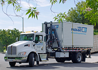 A 1-800-PACK-RAT mini-mover truck drives a portable storage container from a customer's location