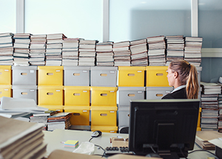 An office worker looks on at a pile of documents and filing boxes