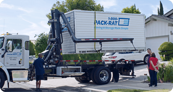 A 1-800-PACK-RAT driver offloads a portable storage container in a customer's driveway as they watch the process