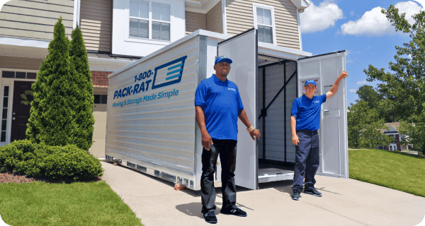 Two 1-800-PACK-RAT employees stand in front of an open portable storage container in a townhome's driveway