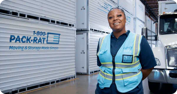 A 1-800-PACK-RAT driver stands in front of her mobile mini truck inside a 1-800-PACK-RAT storage facility surrounded by portable storage containers