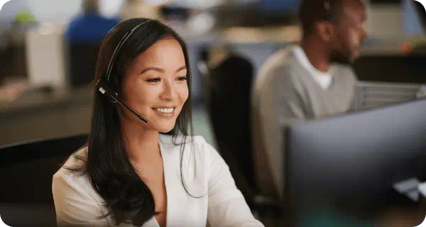 A customer service agent sitting at her computer smiles as she speaks to a customer on the phone