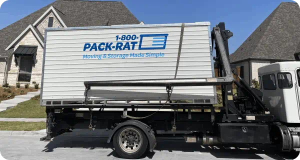 A 1-800-PACK-RAT portable storage container sits on the back of a mini-mover truck in a neighborhood