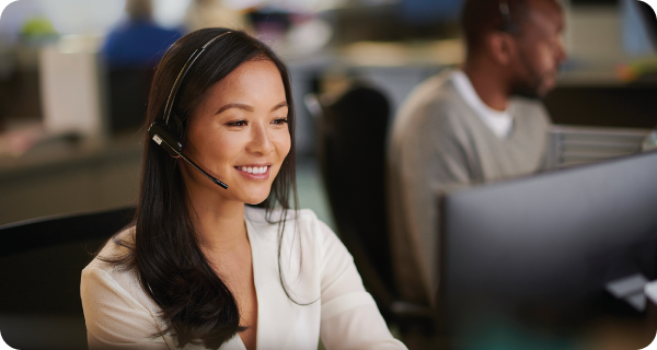 A happy customer service representative sits at a computer in an office environment