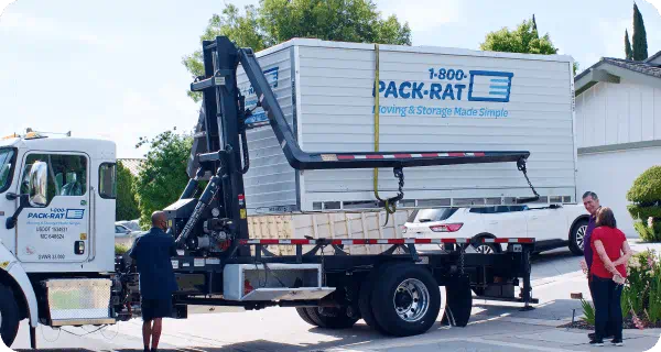 A 1-800-PACK-RAT delivery truck drops off a portable storage container to a pair of customers in their driveway