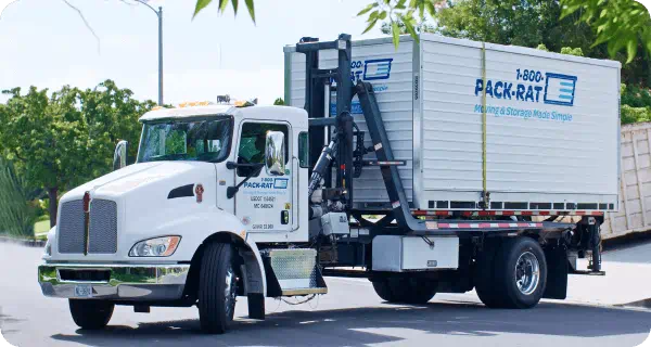 A 1-800-PACK-RAT portable storage container sits on the back of a delivery truck going to a customer's house