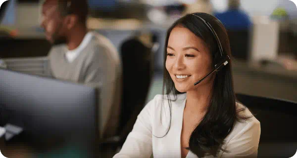 A woman is sitting at a desk with a headset on talking happily with a customer on the phone