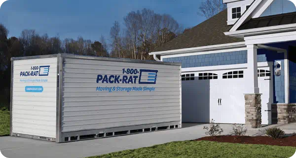 A 1-800-PACK-RAT portable storage container sits in front of a home in the driveway