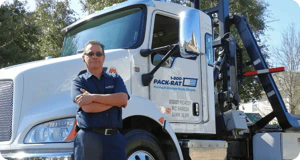 A confident 1-800-PACK-RAT driver stands next to his empty truck with his arms crossed