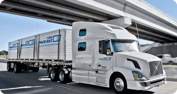 A long-haul truck is driving down a highway, transporting three 1-800-PACK-RAT portable storage containers