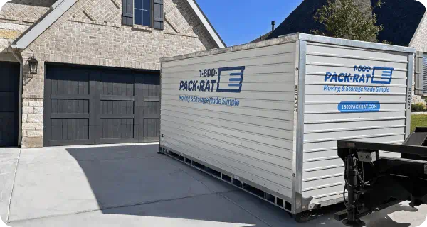 A 1-800-PACK-RAT portable storage container sits in front of a nice home's garage in the driveway