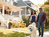 A couple walks their dog on a neighborhood sidewalk