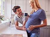 A pregnant woman and her husband talk in their kitchen