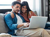 A couple happily looks at their laptop at their home