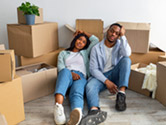 A couple sits on the floor frustrated and surrounded by moving boxes