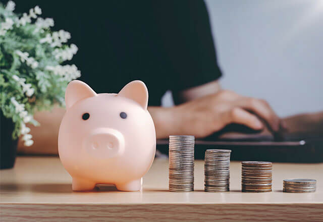 A piggy bank sits on a desk next to stacks of coins