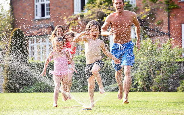 A happy family plays in the yard with a sprinkler