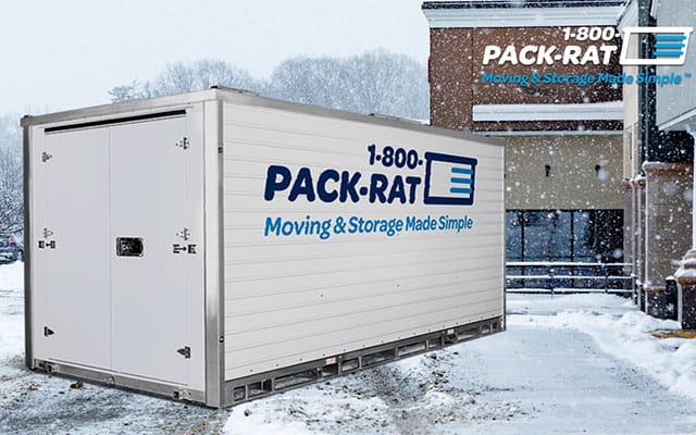 A 1-800-PACK-RAT portable storage container sits in a snowy and icy business parking lot with the 1-800-PACK-RAT logo in the upper right-hand corner of the image