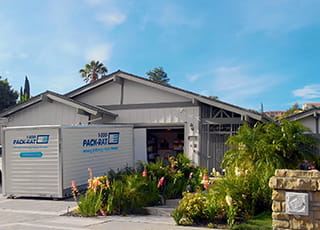 A 1-800-PACK-RAT portable storage container sits in the driveway of a home