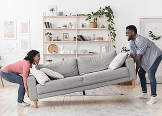 A couple begins to lift and carry their home's couch