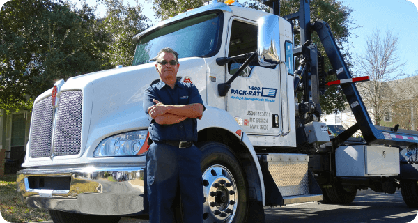 A confident 1-800-PACK-RAT mobile mini truck driver stands next to his truck with his arms crossed