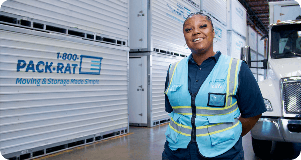 A 1-800-PACK-RAT driver stands in front of her mobile mini truck inside a 1-800-PACK-RAT storage facility surrounded by portable storage containers