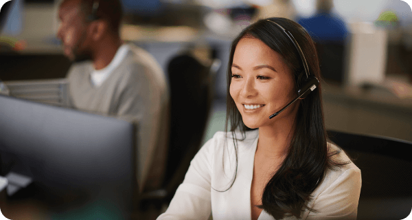 A woman sits at an office desk in front of a computer with a headset on