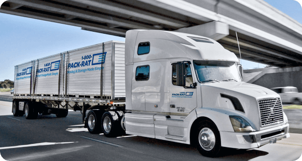 A long-haul 1-800-PACK-RAT truck drives down an interstate highway with three portable storage containers on the back of the trailer