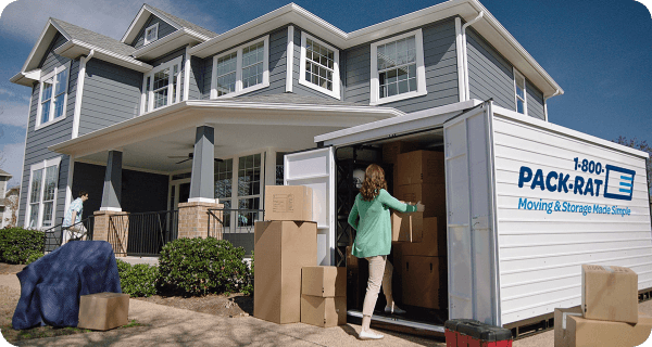 A woman packs boxes into an open 1-800-PACK-RAT container sitting in her home's driveway